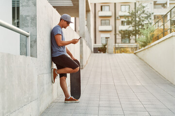 Skater using smartphone while leaning against wall in city