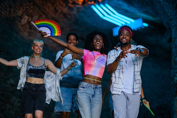 Fototapeta premium Friends dancing together at music festival, celebrating with rainbow fan