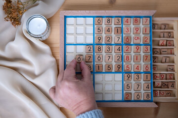 female hands placing number into Sudoku puzzle, solving puzzle on wooden board, brain workout,...