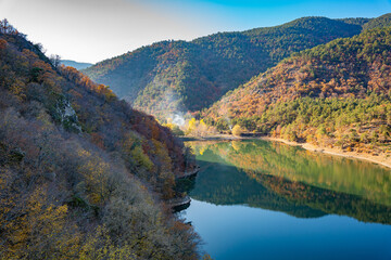 Autumn reflections landscape on calm waters of Boraboy Lake Nature Park. Scenic forest hills and tranquil lake in fall. Peaceful scene with trees and blue sky background. Seasonal change