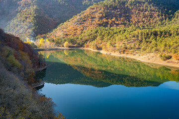 Autumn reflections landscape on calm waters of Boraboy Lake Nature Park. Scenic forest hills and tranquil lake in fall. Peaceful scene with trees and blue sky background. Seasonal change