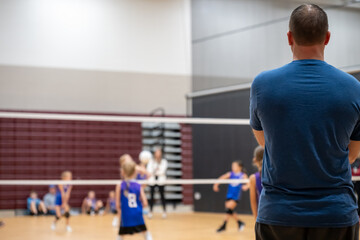 Selective focus behind a coach at a youth volleyball match, blurred game.
