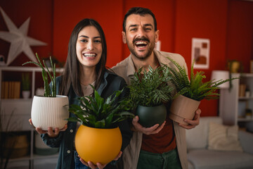 portrait of young happy couple hold flower pots at home