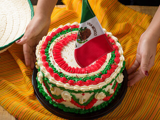 Female hands holding a vibrant and elaborately decorated cake, featuring the Mexican flag design