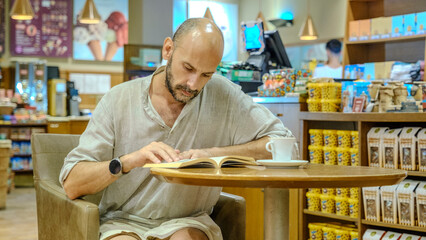 A charismatic middle-aged man wearing a shirt is sitting in a lovely café on a summer evening, enjoying reading a book