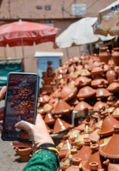 Hand with a mobile phone taking a photo of a set of tagines displayed in street