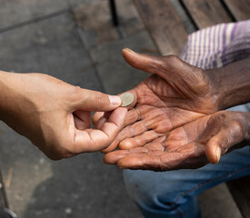 Close-up of hands, one giving money to the other hand of a homeless man - Concept of poverty,...