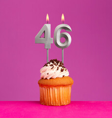 Birthday candle number 46 with cupcake on violet background.