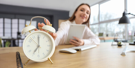 Young businesswoman with tablet computer and alarm clock on table in office, closeup. Time...