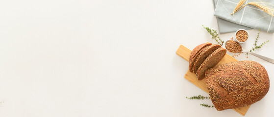 Wooden board with sliced loaf of bread, wheat spikelets, grains and thyme on white background