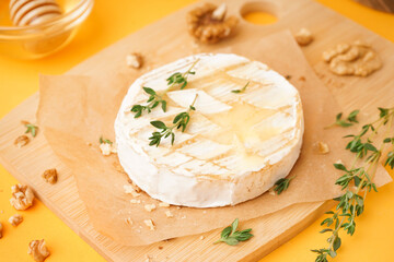 Wooden board of tasty baked Camembert cheese on yellow background
