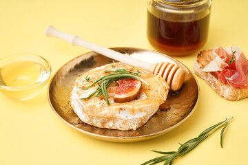 Plate with tasty baked Camembert cheese on yellow background