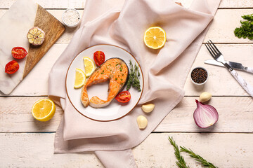 Plate of tasty salmon steak with lemon and tomatoes on light wooden background