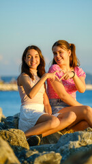 Two teenage girls friends, one slightly overweight and the other with dark skin, chatting and having a great time together by the seaside on a sunny summer day