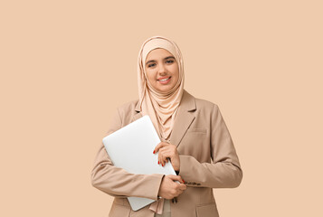 Fototapeta premium Beautiful young Muslim woman in hijab with modern laptop on beige background