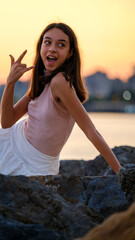 A dark-skinned teenage girl posing cutely while sitting on rocks by the seaside on a sunny summer day