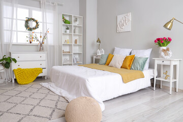 Interior of light bedroom with Easter wreath and tables