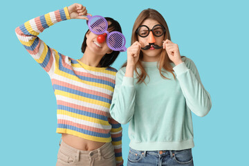 Beautiful young women in funny disguise on blue background. April Fools Day celebration