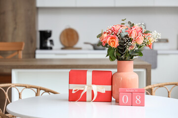 Calendar with date of International Women's Day, gift box and flowers on dining table in kitchen