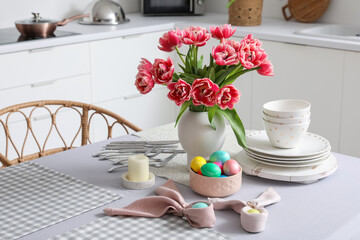 Vase with tulips, Easter eggs and dinnerware on dining table in kitchen