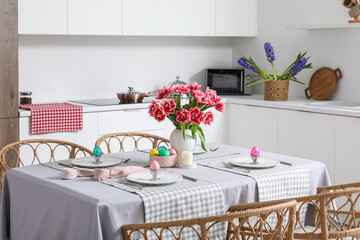 Dining table set for Easter with eggs and tulips in kitchen