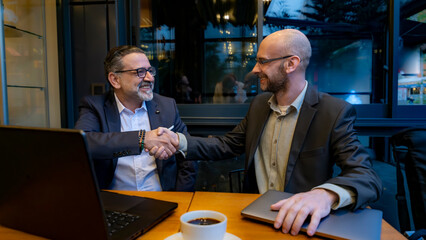 Two middle-aged businessmen, are having a meeting outside the office in a cafe environment, working...