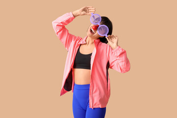 Obraz premium Young smiling female fitness trainer with funny glasses on beige background. Fool's day