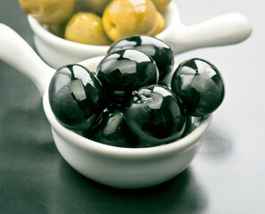 Black olives on a white spoon with green olives in the background for culinary display
