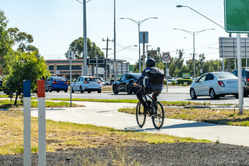 A cyclist wearing a helmet rides along a dedicated bike path near a busy intersection on an urban...