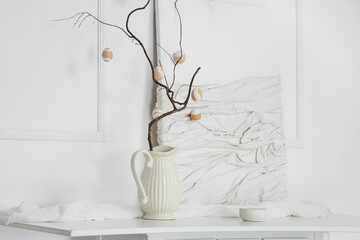 Vase with tree branches, Easter eggs and painting on table near light wall