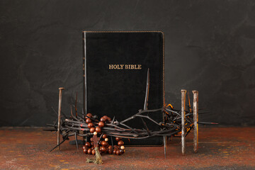 Crown of thorns with Bible, nails and beads on rusty table against black grunge background. Good...