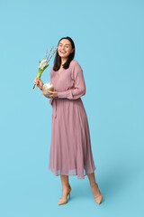 Happy young woman with sweet Easter cake, beautiful flowers and willow branches on blue background