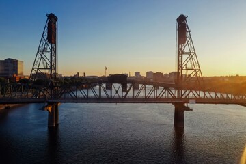 Fototapeta premium Sunrise over the Willamette River and the iconic Hawthorne Bridge in Portland, Oregon. Steel structure, calm water, city skyline. Portland, Oregon, USA
