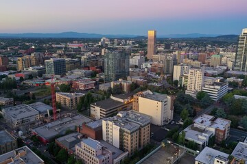 High-angle view of Portland, Oregon's downtown skyline at twilight. Modern and historic buildings, construction crane, and city streets are visible. Oregon, USA