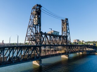Elevated train cars cross the historic Steel Bridge over the Willamette River. Industrial cityscape in the background. Portland, Oregon, USA