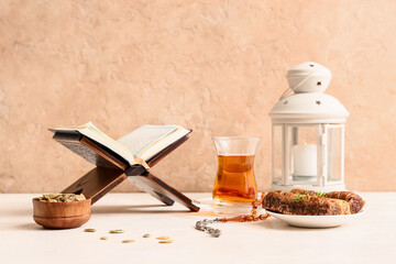 Koran, baklava, glass cup of tea and lantern on white table against beige background. Ramadan celebration