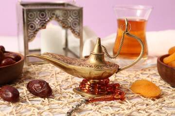 Aladdin lamp, prayer beads and dried apricots on white table against lilac background. Ramadan celebration