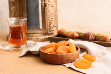 Dried apricots, glass cup of tea and Muslim lantern on beige table, closeup. Ramadan celebration