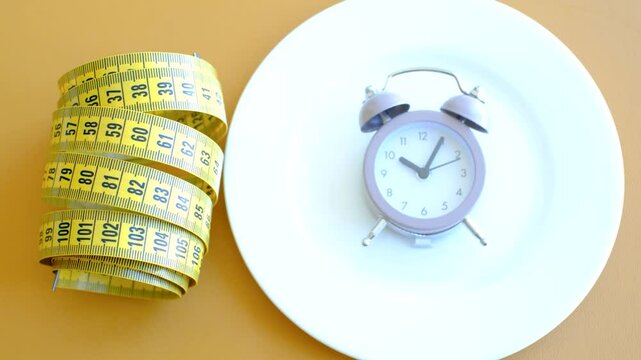 Empty plate with alarm clock and measuring tape on brown background close-up top view.