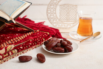 Dates, Koran, prayer carpet and glass cup of tea on white table against wooden background. Ramadan celebration