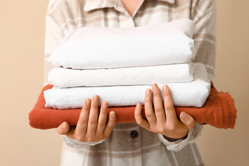 Young woman holding stack of clean bed sheets near beige wall, closeup