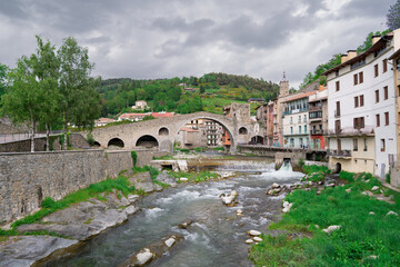 Fototapeta premium Puente medieval sobre un rio en una ciudad pintoresca de los pirineo, un día soleado con cielo azul y nubes. Desde Camprodon, Gerona, Cataluña, España.