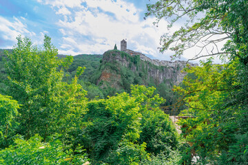 Pueblo medieval en las monta&ntilde;as sobre un acantilado de roca y mucha vegetaci&oacute;n un d&iacute;a soleado con cielo azul y nubes. Desde Castellfollit de la Roca, Gerona, Catalu&ntilde;a, Espa&ntilde;a, Europa.