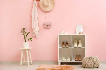 Stand for shoes and pouf near pink wall in interior of hallway