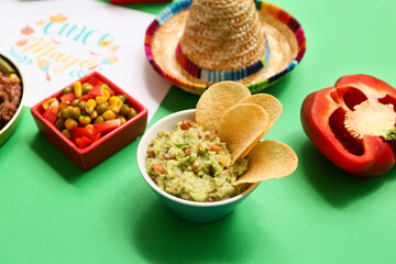 Bowl with traditional Mexican guacamole and potato chips on green background, closeup. Cinco de Mayo (Fifth of May) celebration