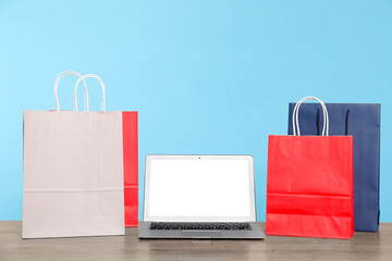 Internet shopping. Laptop and colorful paper bags on wooden table against light blue background