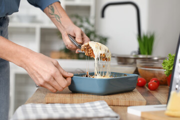Woman with spatula taking piece of delicious lasagna from baking dish in kitchen