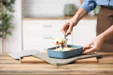 Woman with spatula taking piece of delicious lasagna from baking dish in kitchen