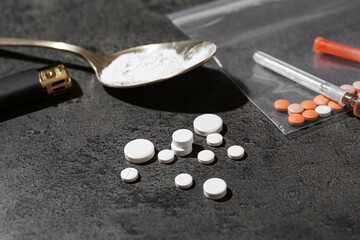 Drug addiction. Spoon with powder, pills, cigarette lighter and syringe on gray textured table,...