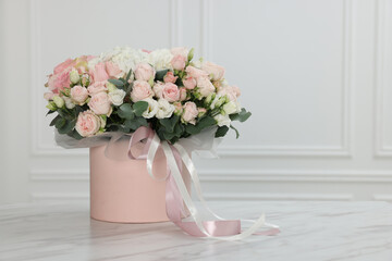 Gift box with bouquet of beautiful flowers and eucalyptus branches on marble table against white wall. Space for text